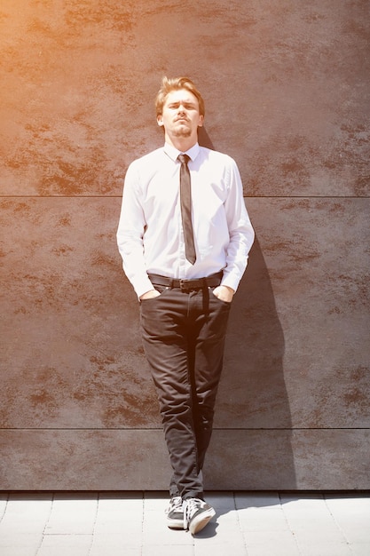 retrato de un nuevo hombre de negocios con una camisa blanca y una corbata negra parado frente a una pared gris afuera