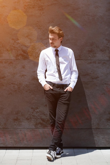 retrato de un nuevo hombre de negocios con una camisa blanca y una corbata negra parado frente a una pared gris afuera