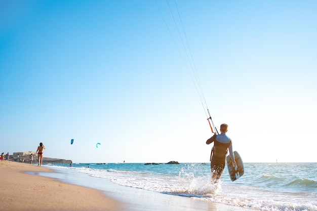 Retrato onda kitesurfista caminhando na praia com sua prancha e pipa