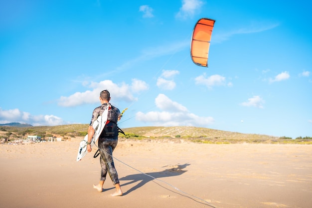 Retrato onda kitesurfista caminhando na praia com sua prancha e pipa