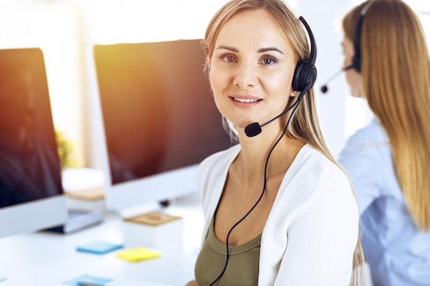 Retrato del operador del centro de llamadas en el trabajo en una oficina soleada. Grupo de personas con auriculares listos para ayudar a los clientes. Concepto de negocio.