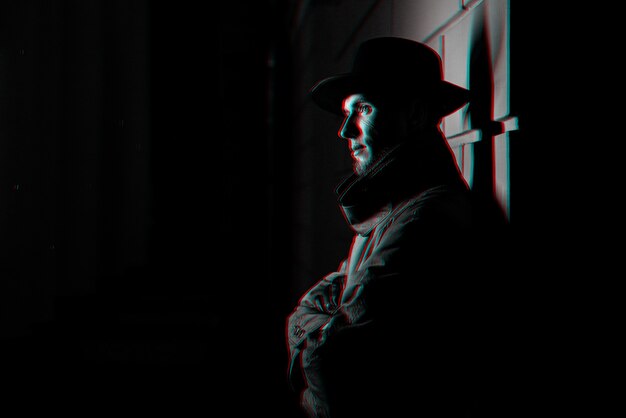 Retrato oscuro de un hombre con un impermeable con sombrero por la noche en la calle. Blanco y negro con efecto de realidad virtual 3D glitch