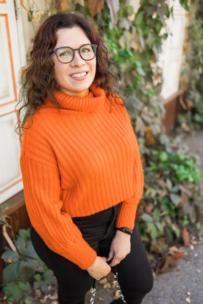 Retrato otoñal de una mujer joven atractiva con gafas elegantes en un swea naranja de moda de punto