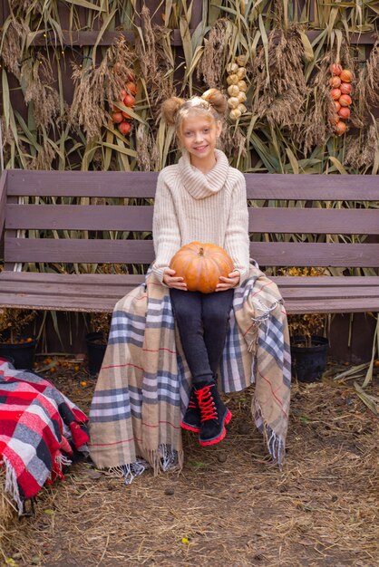 retrato de otoño de una hermosa niña con una calabaza en halloween cerca de la casa