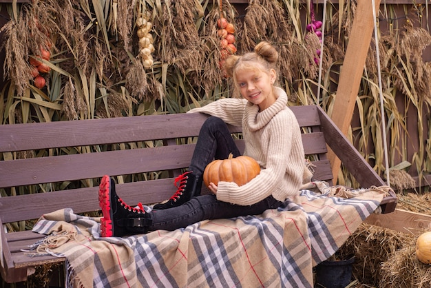 retrato de otoño de una hermosa niña con una calabaza en halloween cerca de la casa