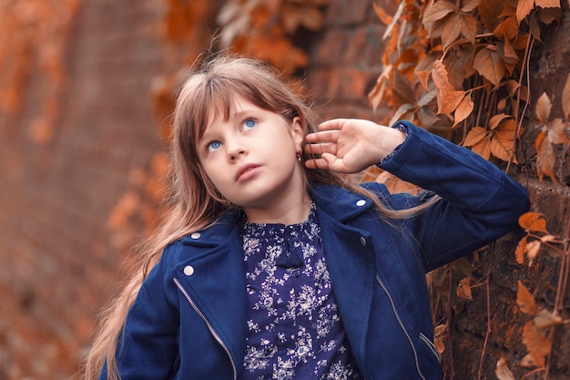 Retrato de otoño hermosa niña cerca de un muro de piedra se ve de lado soñadora