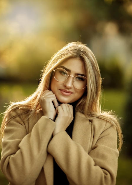 Retrato de otoño. Mujer elegante alegre con gafas de imagen y abrigo en el parque