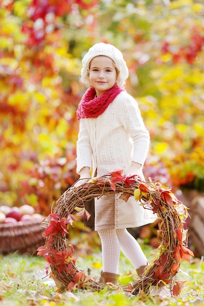 Retrato de otoño de niña linda. Niña bonita con guirnalda de hojas de parra roja en el parque de otoño.