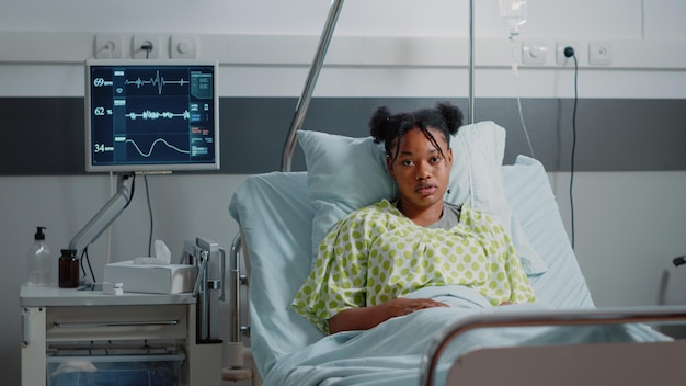 Retrato de un paciente joven en la cama con una bolsa de goteo IV, esperando que el médico brinde asistencia médica y cure la enfermedad. Mujer enferma sentada en la sala del hospital con monitor de frecuencia cardíaca para sanar