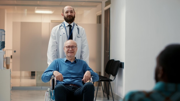 Retrato de un paciente jubilado con discapacidad física y discapacidad, médico masculino que ayuda con el transporte de sillas de ruedas. Hombre mayor paralizado que sufre de una condición de salud crónica.