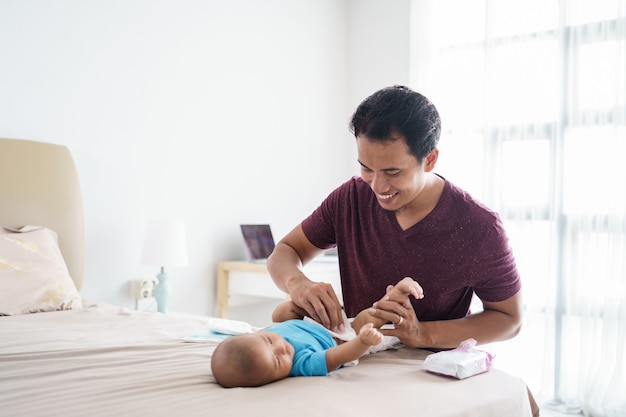 Retrato de padre asiático cambiando el pañal de su bebé infantil en casa