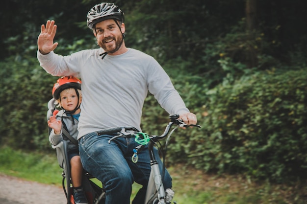 Retrato de padre e hijo agitando en bicicleta contra las plantas