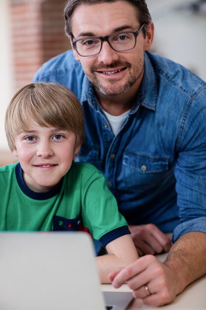 Retrato de padre e hijo usando laptop en la cocina