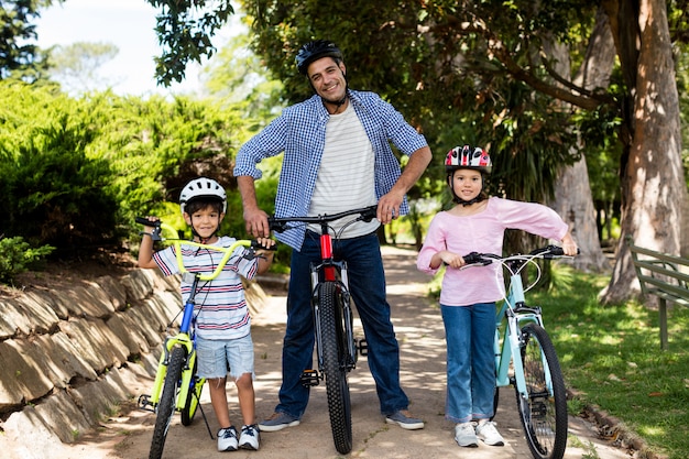 Retrato de padre e hijos de pie con bicicleta en el parque