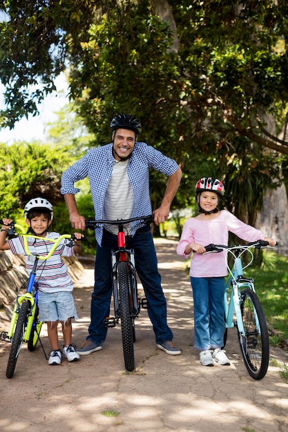 Retrato de padre e hijos de pie con bicicleta en el parque