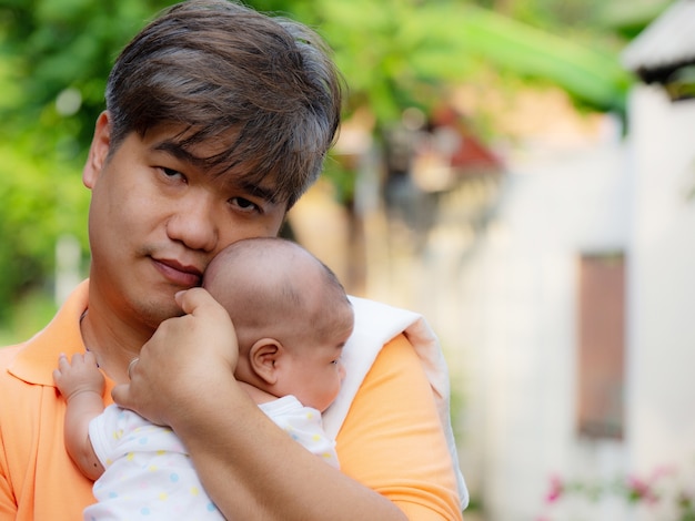 Retrato del padre feliz de Asia que detiene a su bebé dulce recién nacido vestido en la ropa blanca.