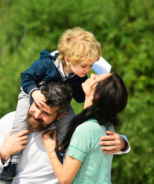 Retrato de un padre feliz dando a su hijo un paseo a hombros abrazando a su esposa y mirando hacia arriba