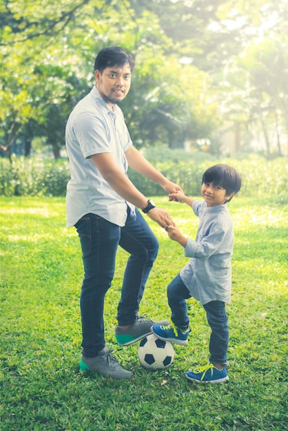 Foto retrato de un padre con su hijo de pie con una pelota de fútbol en el parque