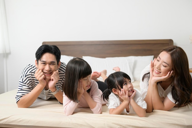 Retrato de padres asiáticos con dos hijas pequeñas en la cama en el concepto de familia feliz del dormitorio