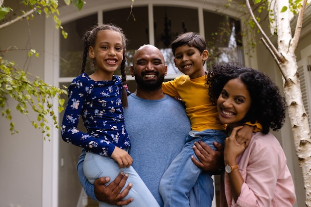 Foto retrato de padres bi-raciales felices sosteniendo a su hijo e hija, abrazándose en el jardín afuera de la casa. familia, amor, unión, hogar, estilo de vida y vida doméstica, inalterados.