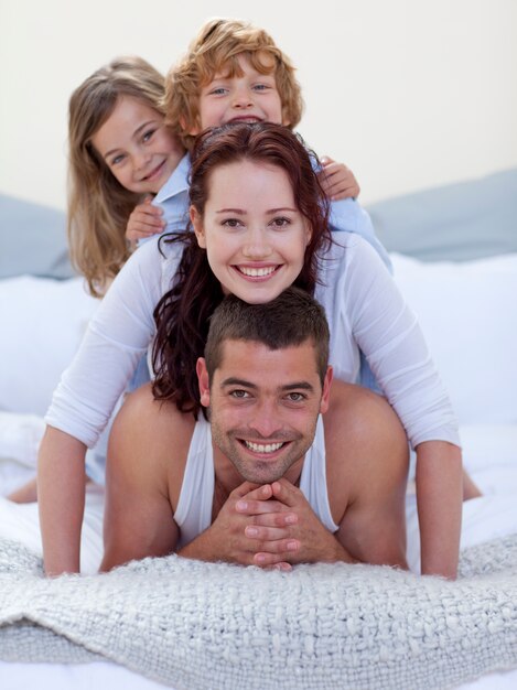 Foto retrato de padres felices y niños divirtiéndose en la cama