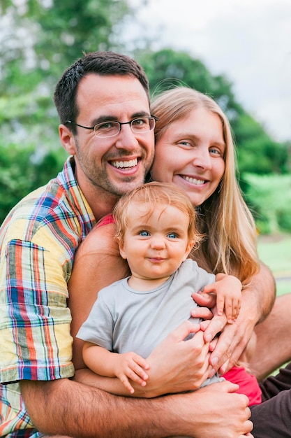 Foto retrato de padres sonrientes con su hija sentada en el parque