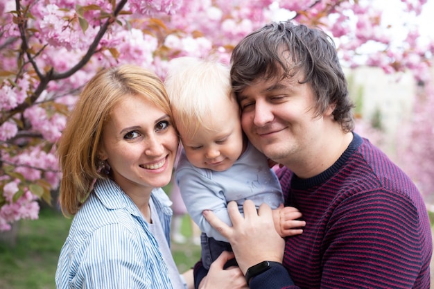 Retrato de padres con su hijo en la primavera cerca de la cereza japonesa sakura se encuentra con la primavera Sakura florece muy bellamente con flores rosas