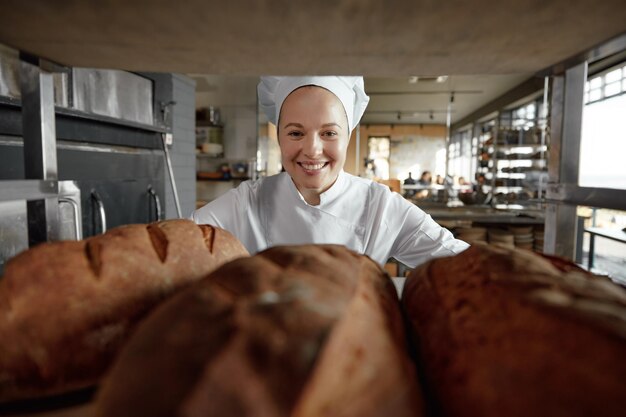 Foto retrato de una panadera sonriente mirando a través de un estante con panes recién horneados