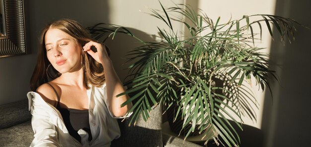 Foto retrato de pancarta de una mujer joven y hermosa cerca de la ventana con la sombra de las flores en su espacio de copia de la cara estética primaveral de la mañana