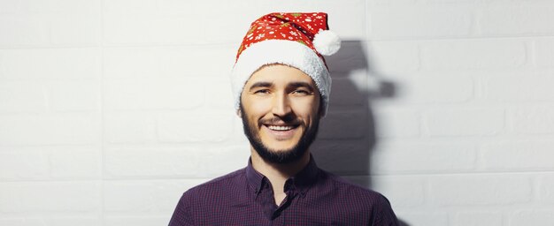 Foto retrato panorámico de joven sonriente, con sombrero de santa sobre fondo de pared de ladrillo blanco.