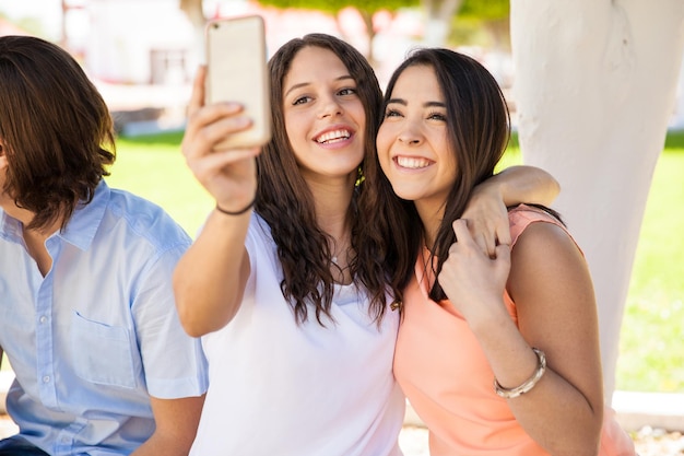 Retrato de un par de amigas hispanas tomándose una selfie con un smartphone en la escuela