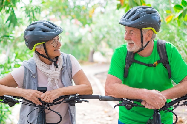 Retrato de un par de ancianos y felices enamorados mirándose unos a otros sonriendo y divirtiéndose con sus bicicletas en la naturaleza al aire libre juntos sintiéndose bien y saludablesxA