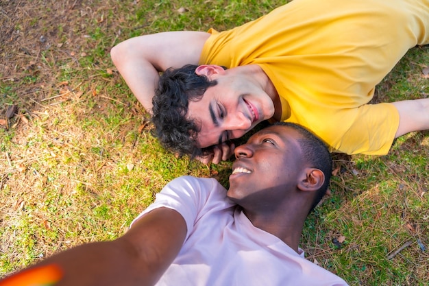 Retrato de un par de hombres multiétnicos en un parque concepto lgbt tirados en el césped tomando una selfie