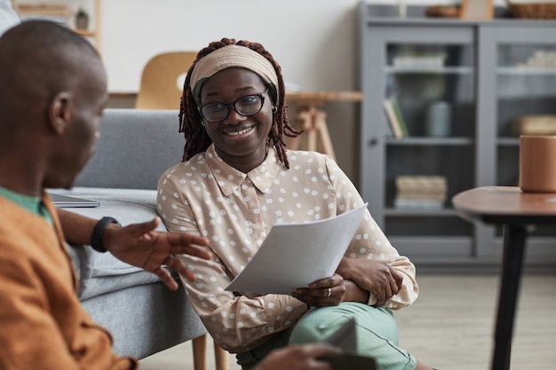 Retrato de una pareja afroamericana moderna que trabaja desde casa juntos, se centran en la mujer joven sonriente que sostiene el documento mientras está sentado en el piso, espacio de copia