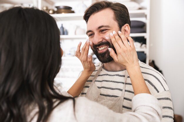 Retrato de pareja alegre hombre y mujer de 30 años vistiendo delantales divirtiéndose juntos mientras se cocina en la cocina de casa