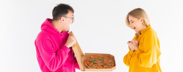 Retrato de pareja alegre hombre y mujer en suéteres de colores sonriendo mientras come pizza
