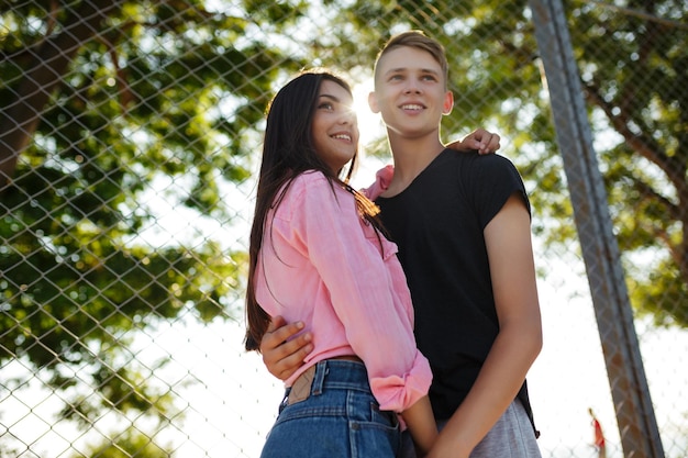 Retrato de una pareja alegre de pie y abrazándose mientras miran soñadoramente a un lado en el parque