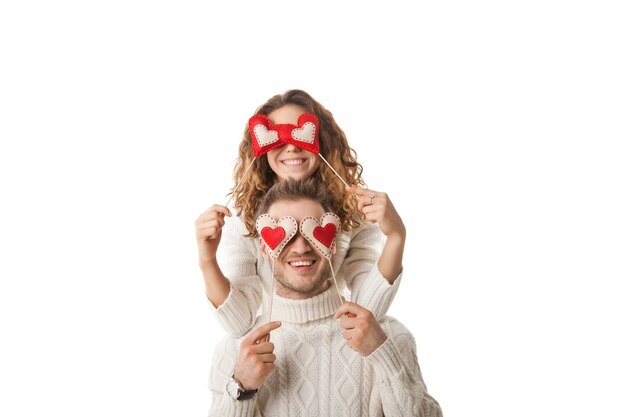 Retrato de pareja alegre sosteniendo corazones rojos por sus ojos y riendo