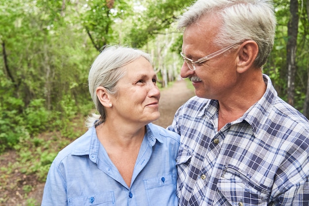 retrato, de, pareja anciana, enamorado, sonriente, y, abrazar, con, el telón de fondo, de, árboles verdes