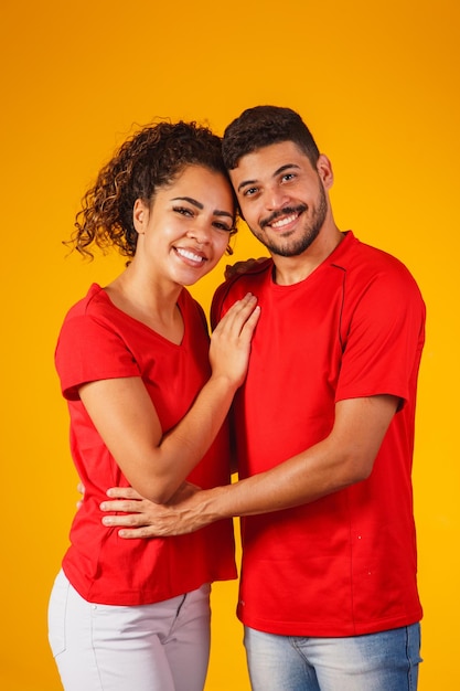 Foto retrato de una pareja de contenido con ropa básica sonriendo a la cámara mientras una mujer pone su cabeza en el hombro masculino aislada sobre un fondo amarillo, él está sorprendido y feliz