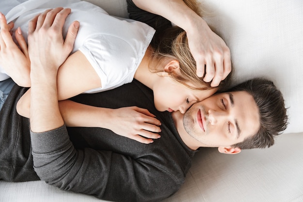 Retrato de pareja encantadora hombre y mujer abrazándose juntos mientras está acostado en el sofá en una habitación luminosa en casa