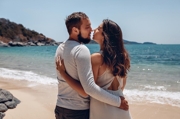 Retrato de una pareja fabulosa posando en una playa de arena junto a un mar tropical brillante, mirándose con ojos amorosos. concepto romántico.