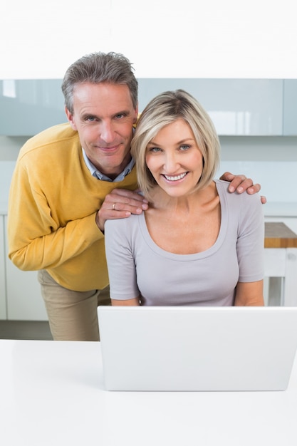 Retrato de una pareja feliz con la computadora portátil en la cocina