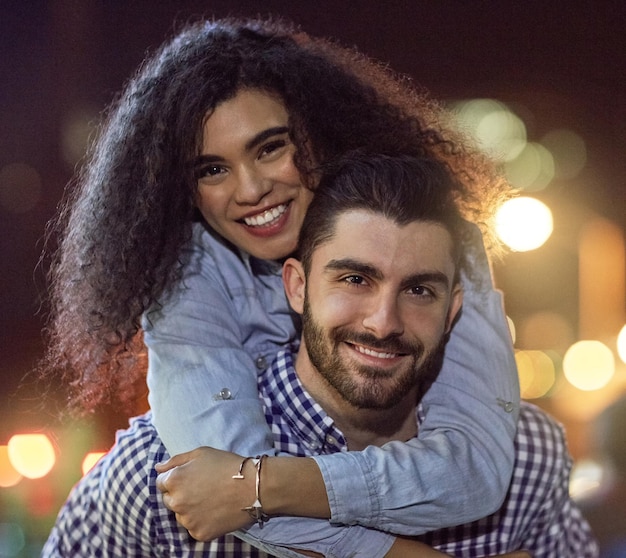 Retrato de pareja feliz y noche con abrazo en la ciudad para el cuidado del amor o al aire libre abrazar juntos hombre joven mujer o amantes con sonrisa o luces a última hora de la noche para la unión o el afecto en una ciudad urbana