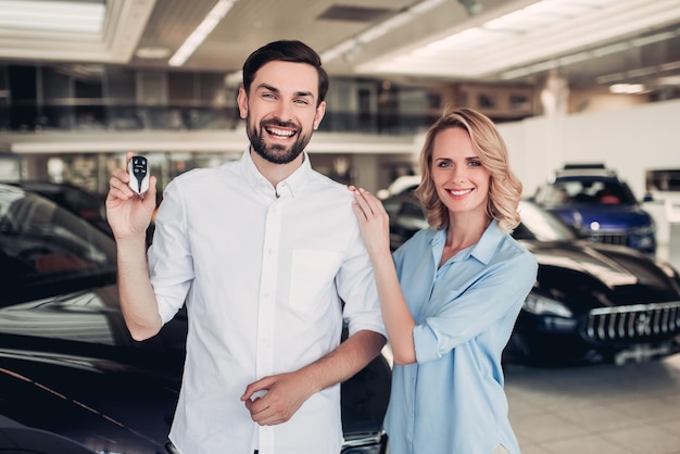 Retrato de una pareja feliz sosteniendo las llaves de un auto nuevo en el salón del concesionario