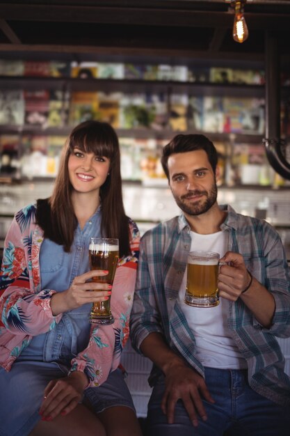 Retrato de pareja feliz sosteniendo vasos de cerveza en el mostrador