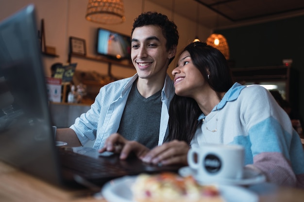 Retrato de una pareja feliz usando la computadora portátil en un café.