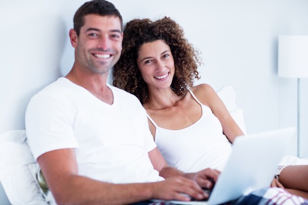 Retrato de una pareja feliz usando la computadora portátil en la cama