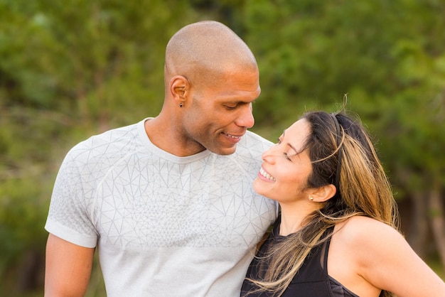 Retrato de pareja de fitness abrazándose y mirando el uno al otro. Pareja multiétnica haciendo ejercicio al aire libre.