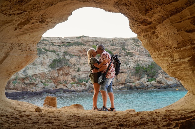 Retrato de pareja heterosexual senior besándose en la cueva de una isla Amor en San Valentín de verano